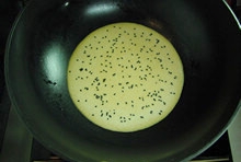 等到鍋內的蛋餅表面開始凝固的時候，再撒上一層熟黑芝麻；
