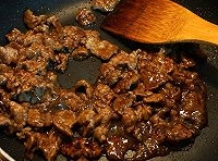 用大火翻炒牛肉片至變色后，倒醬油進去炒勻；