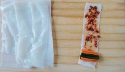 取上一段米皮，在米皮上抹上一層芝麻辣醬，到邊上擺上韭菜和胡蘿蔔，再慢慢捲起來即可。