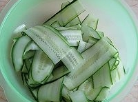 黃瓜洗凈，用削皮刀削成薄片，放入盤裡加點鹽腌制至變軟；