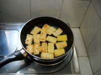 鍋中倒油燒熱，把裹了澱粉的豆腐放入用中火煎至兩面酥黃后盛起；